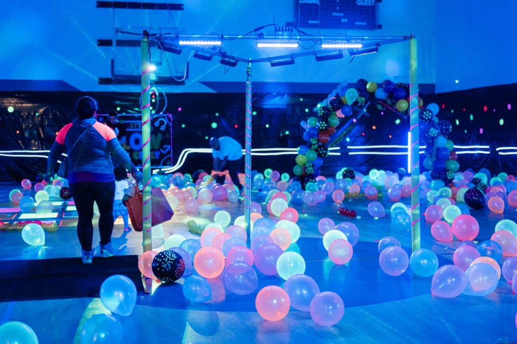 Families exploring the colorful balloon-filled gym at the Crossroads Neon Egg Hunt